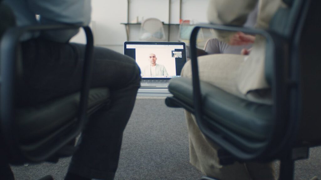 Two adults watching an online consultation on a laptop in a professional office environment.